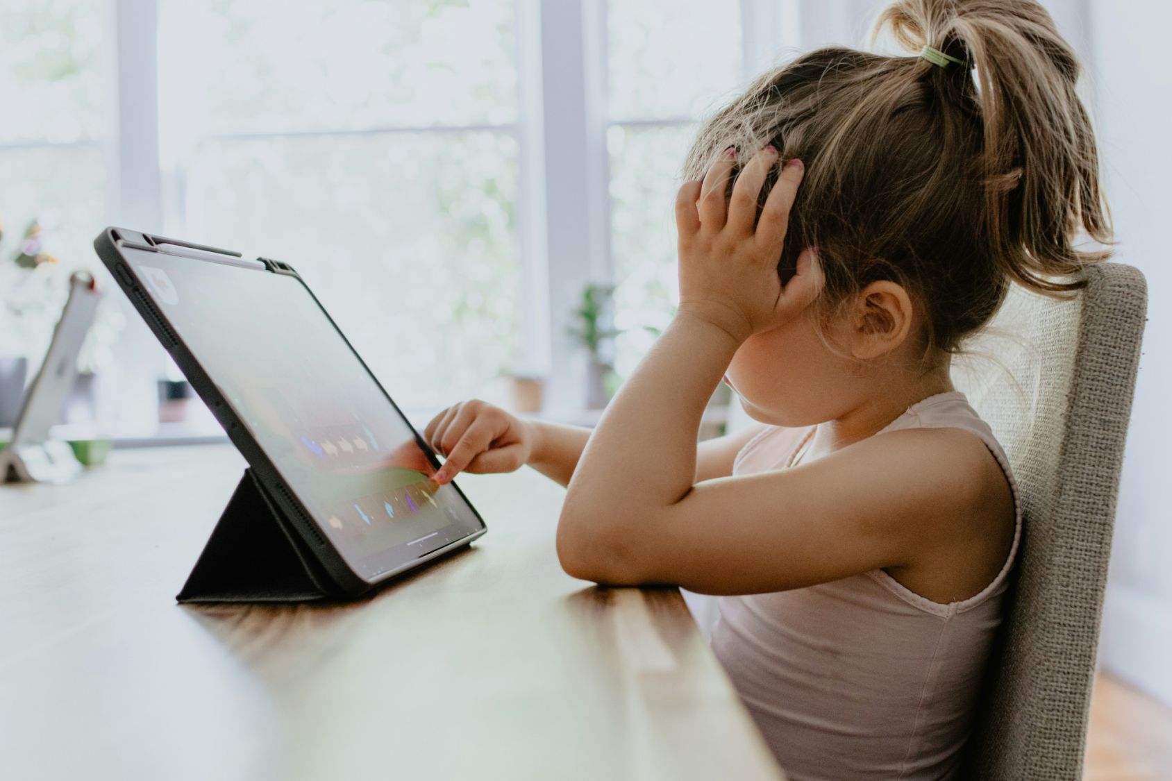 Een geconcentreerd klein meisje dat een tablet gebruikt die op een tafel staat