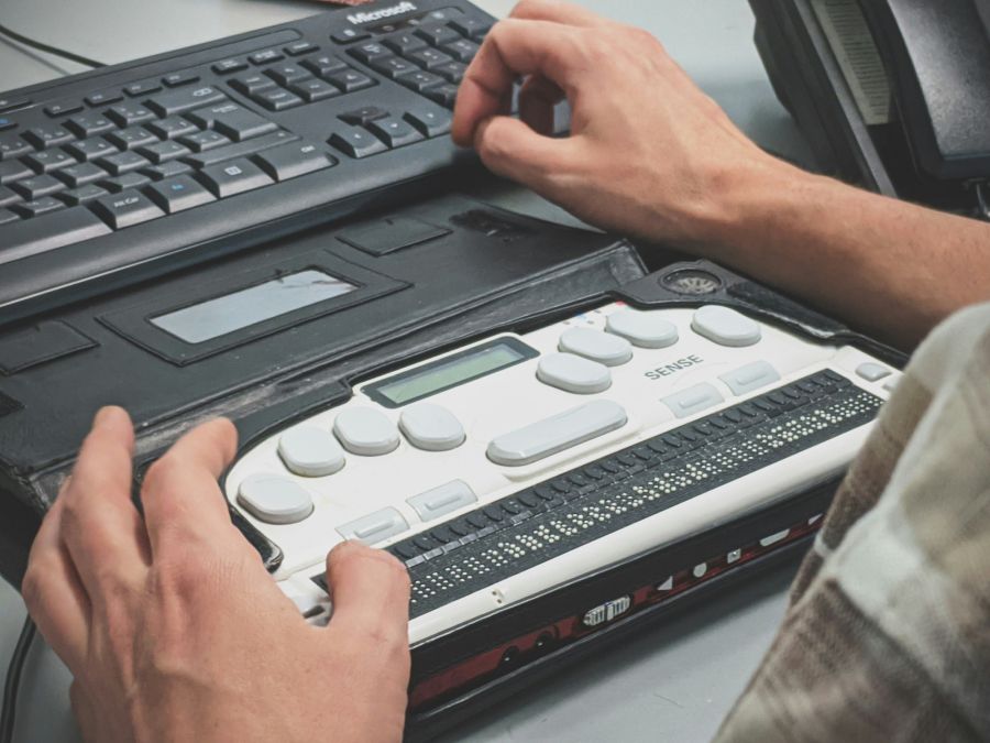 Een persoon die een elektronische brailleleesregel gebruikt die is aangesloten op een computertoetsenbord.