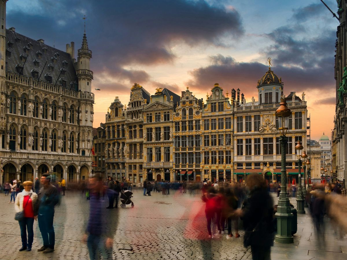 Vue de la Grand-Place de Bruxelles au coucher du soleil avec des bâtiments historiques et des gens qui semblent flous en mouvement